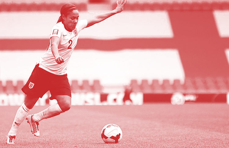 Footballer Alex Scott, kicking the ball at her feet with arms aloft, playing for England in 2014