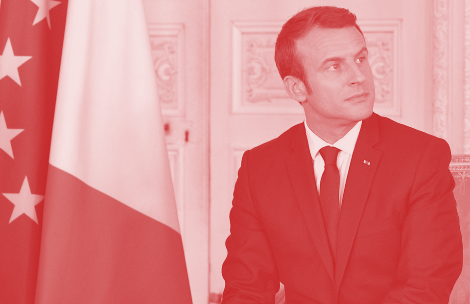 French president Emmanuel Macron looking serious and to the right next to a flag