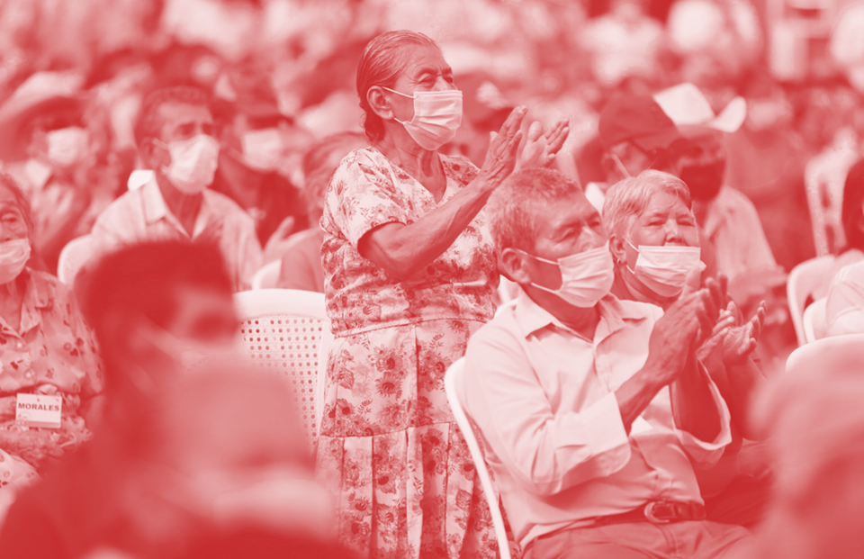 Crowd of people wearing covid-19 masks, mostly clapping and one woman standing up